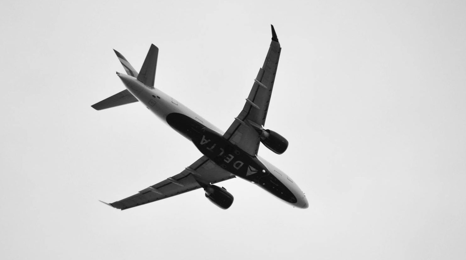 commercial airplane flying overhead in black and white